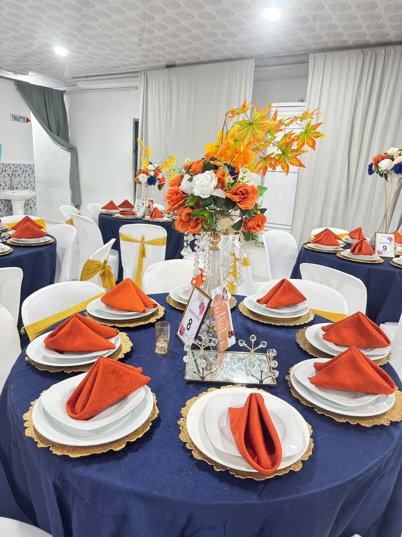 Salle de réception décorée par Belkarann : nappes bleu nuit, serviettes rouille, assiettes dorées et centre de table fleuri